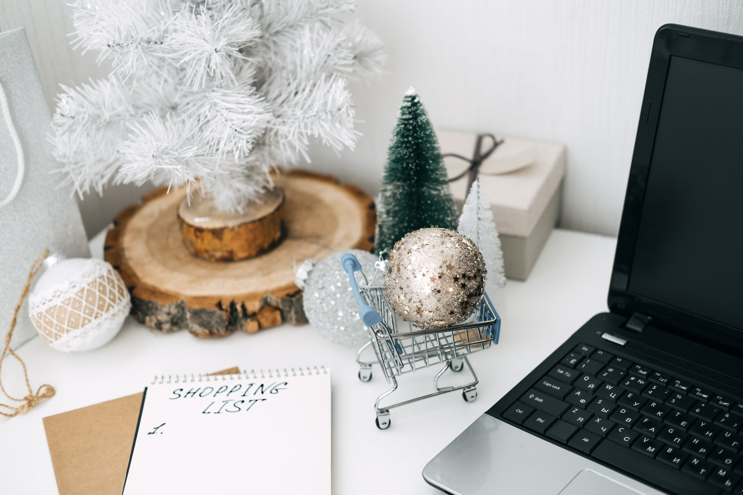 Einkaufsliste für Weihnachtsgeschenke auf einem Schreibtisch mit Laptop.