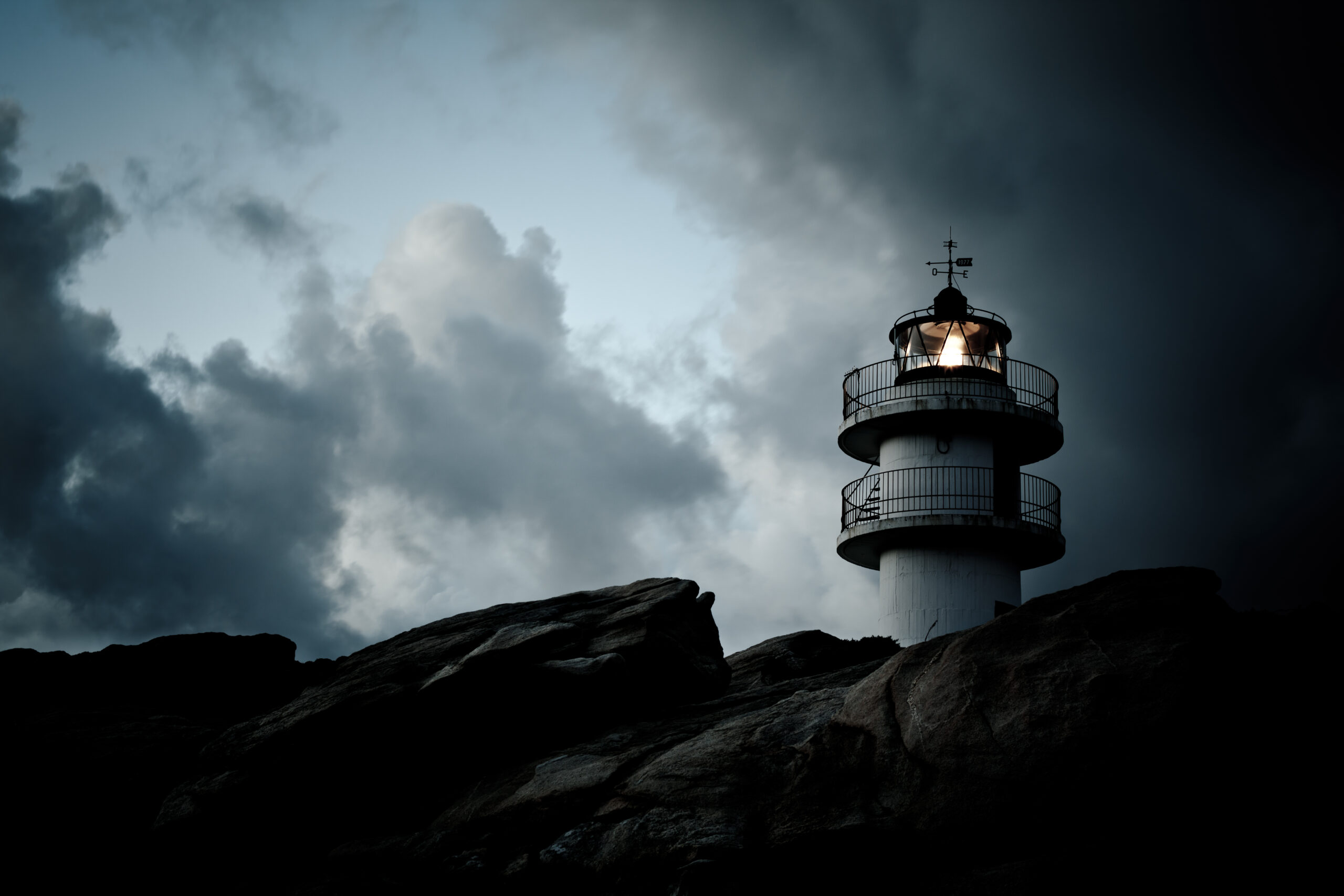 Ein Leuchtturm steht auf einer felsigen Klippe und ist von dunklen Wolken umgeben.